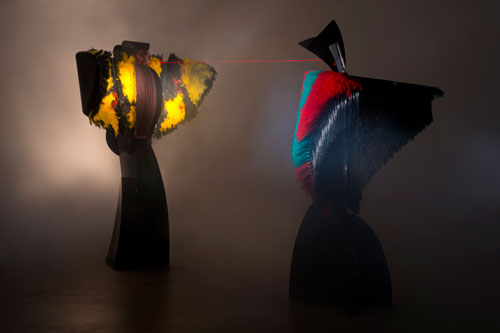 Liliane Lijn. Conjunction of Opposites: Lady of the Wild Things and Woman of War, 1986. Two mixed media performing sculptures enact a computer controlled 6 minute drama which includes movement, song, the transformation of sound to light, and a laser display, 400 x 800 x 400 cm (12 x 24 x 12 ft). First exhibited at the Art and Science Venice Biennale in 1986 in the Art, Technology, and Computers Section in the Arsenale.
